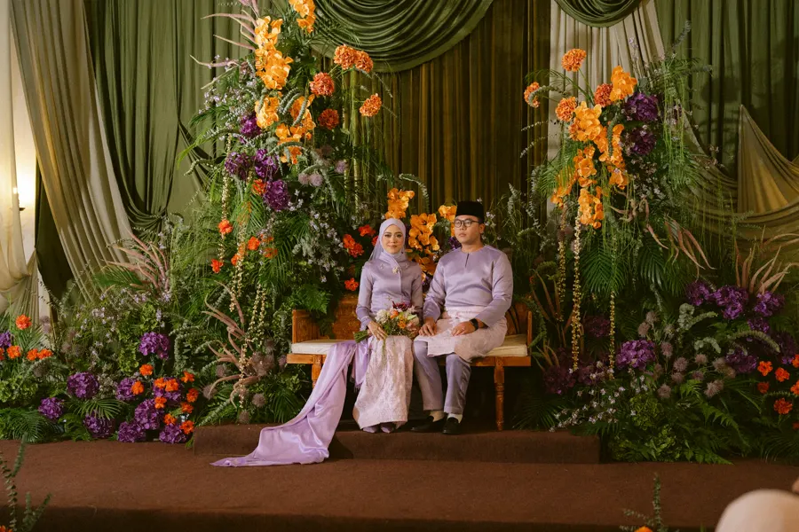 Newlyweds seated against green, orange and purple floral styling