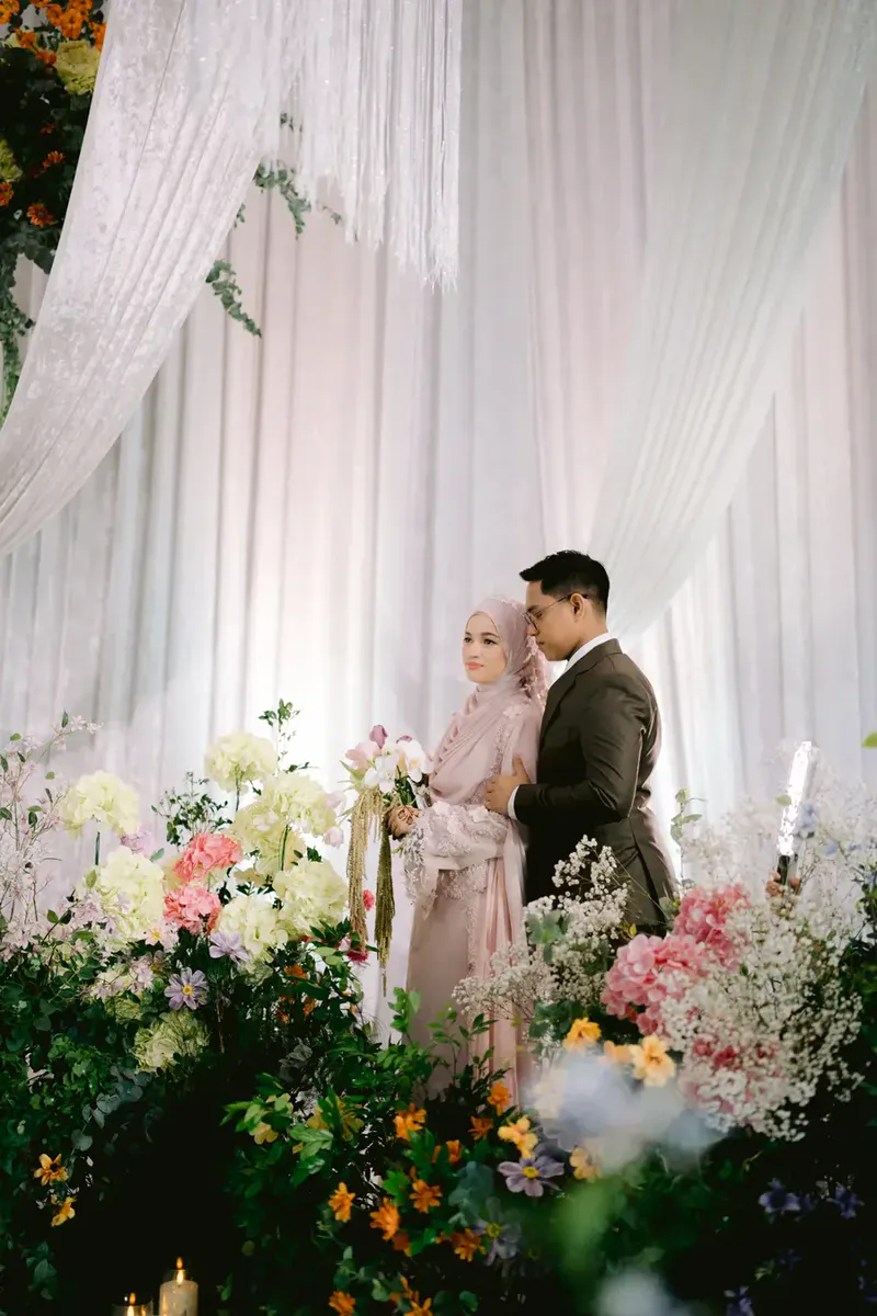 Bride and groom surrounded by pastel flowers in front of white drapes
